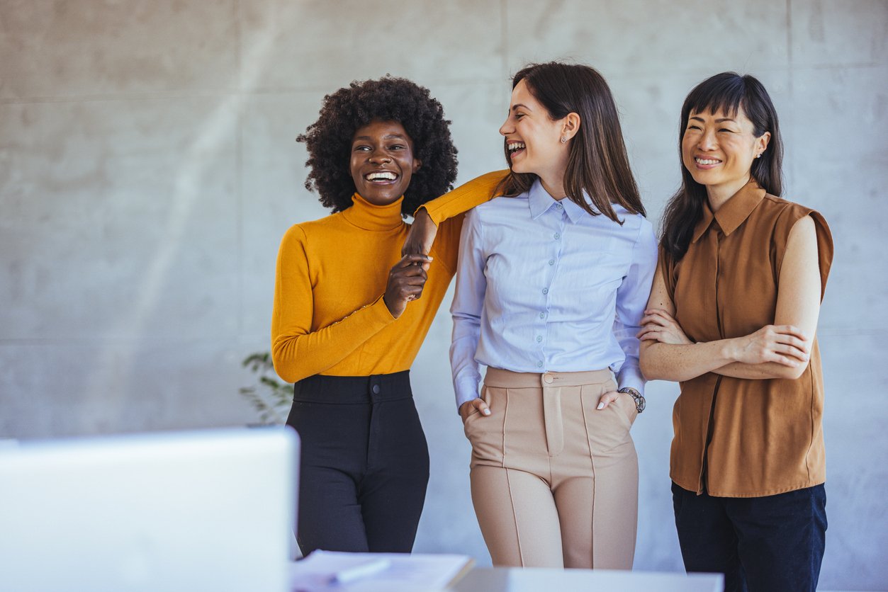 Three professional looking women standing in a modern office, smiling and laughing Three professional looking women standing in a modern office, smiling and laughing